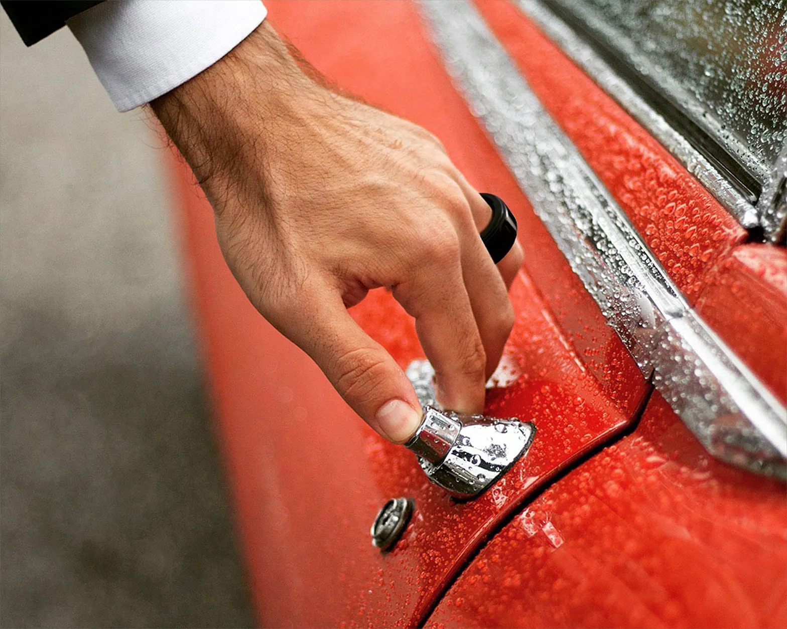 The HB Ring in stainless steel, worn in the rain beside a red car